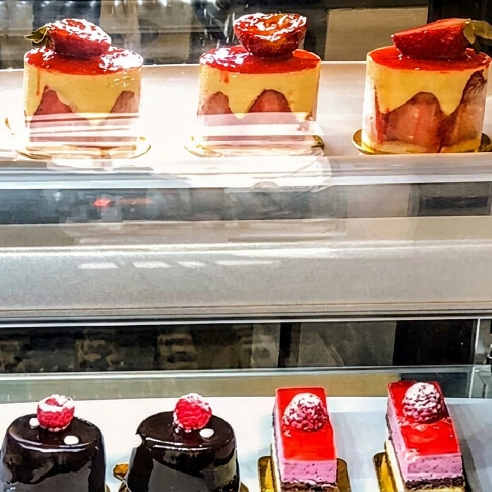 Display case with two shelves of gourmet pastries, including strawberry mousse cakes and chocolate raspberry cakes.